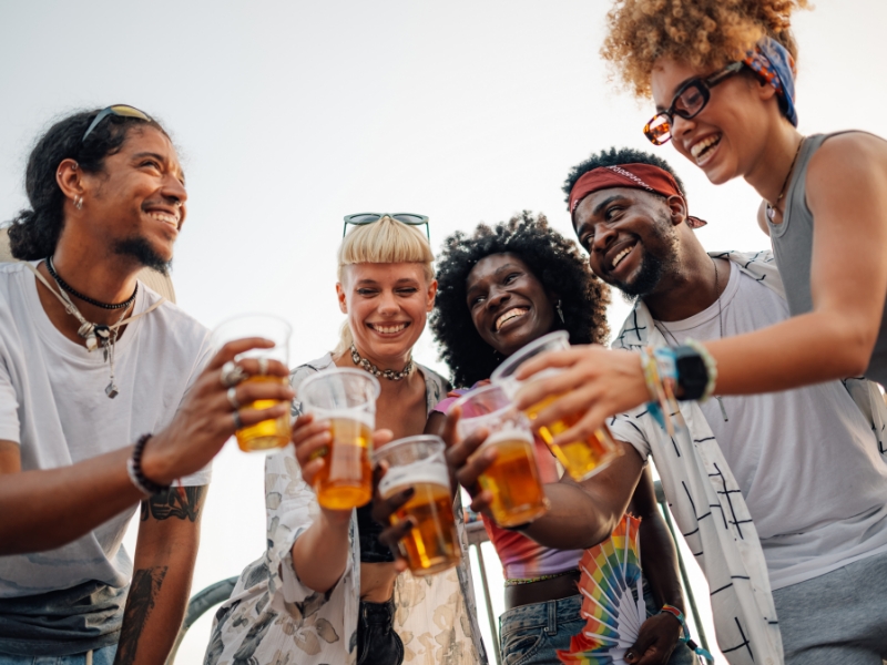 5 Freunde stehen im Halbkreis, lächeln und stoßen mit Bier an